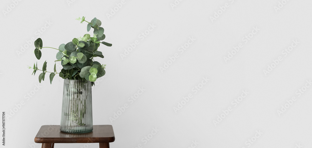 Wall mural Vase with eucalyptus on wooden stool near light wall