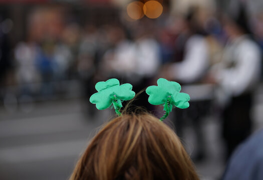 A spectator with her back turned and wearing a shamrock headband watches the St. Patrick's Day parade