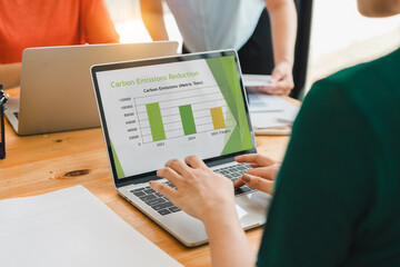 person analyzing carbon emissions reduction chart on laptop screen during collaborative meeting, emphasizing sustainability and al progress