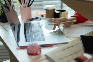 A woman in a red sweater is sitting at a desk with a laptop and a notebook. She is smiling and she...