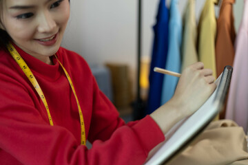 A woman in a red sweater is sitting at a desk with a laptop and a notebook. She is smiling and she...