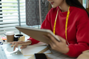 A woman in a red sweater is sitting at a desk with a laptop and a notebook. She is smiling and she...