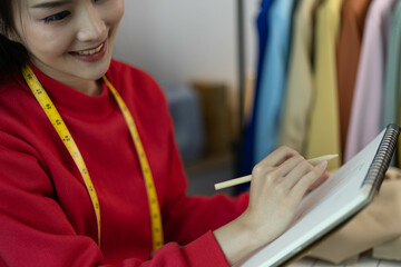 A woman in a red sweater is sitting at a desk with a laptop and a notebook. She is smiling and she...