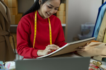 A woman in a red sweater is sitting at a desk with a laptop and a notebook. She is smiling and she...