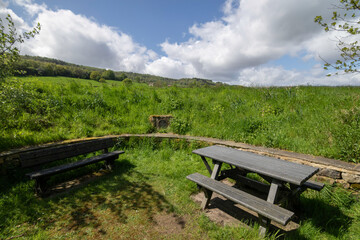 Obraz premium Quite a picnic area with tables and benches facing a green hillside under a brilliant, somewhat cloudless sky, Nidderdale, North Yorkshire, UK.