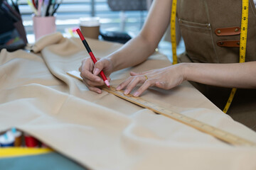 A woman is sewing a piece of fabric and using a ruler to measure it. She is also using a red pen to...