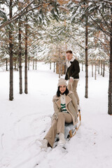 A man and a woman in love ride a sleigh through a snowy forest in winter, relaxing in the countryside during the Christmas holidays. Selective focus