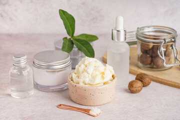 Bowl of shea butter, nuts and cosmetic products on light table