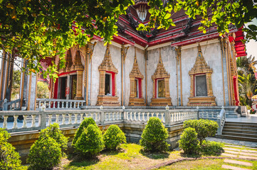 The beautiful facade of the buddhist Wat Chalong temple in Phuket, Thailand behind a small garden and framed by leaves of a tree.