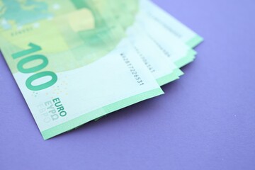 Big amount of one hundred euro money bills on lilac background