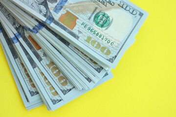 Big amount of hundred dollar bills in thick stack lies on bright yellow color paper background