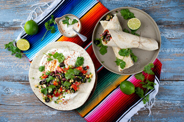 Traditional Mexican style burritos - tortilla wrap with vegetables and cheese served as top view with sour cream chili dressing on a design plate