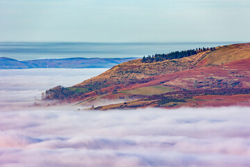 Rural valley filled with thick fog and large hills and farmland rising above