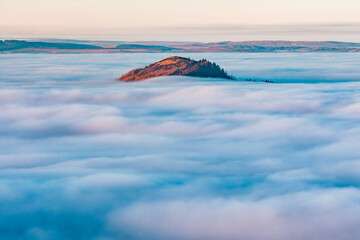 Rural valley filled with thick fog and large hills and farmland rising above