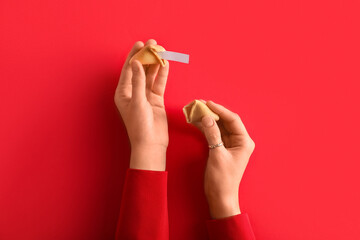 Female hands with broken fortune cookie on red background