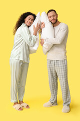 Beautiful young couple in pajamas with soft pillows on yellow background. World Sleep Day