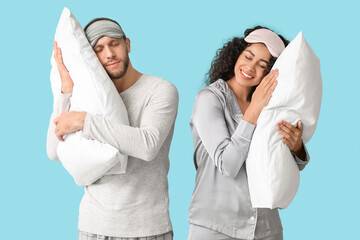 Beautiful young couple in pajamas and masks with soft pillows on blue background. World Sleep Day
