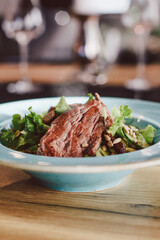 Fresh healthy salad with baked meat, restaurant in the background