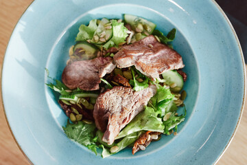 Fresh healthy salad with baked meat, restaurant in the background