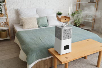 Interior of bedroom with modern humidifier on wooden bench near bed