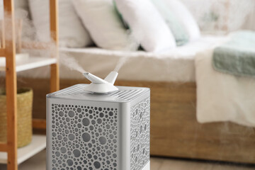 Modern humidifier near bed in bedroom, closeup