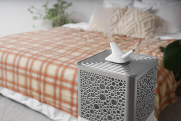 Modern humidifier on floor near big bed in bedroom, closeup