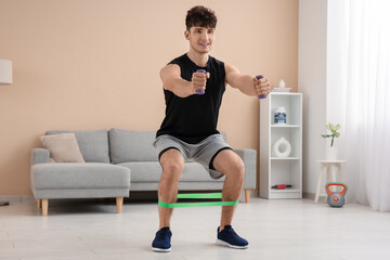 Sporty young man training with elastic band and dumbbells at home