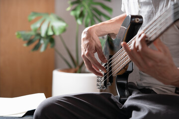 A person sitting on a chair practicing walking technique on electric bass.