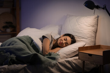 Beautiful young happy woman sleeping on bed in evening at home