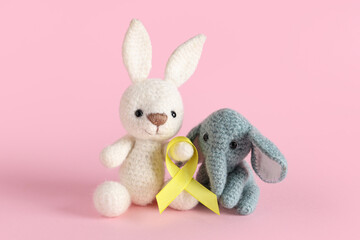Knitted toys and yellow ribbon on pink background. Childhood cancer awareness concept