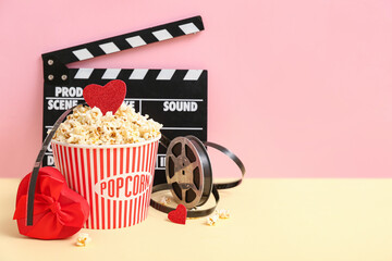 Bucket of popcorn with gift box, film reel and movie clapper on colorful background. Valentine's...