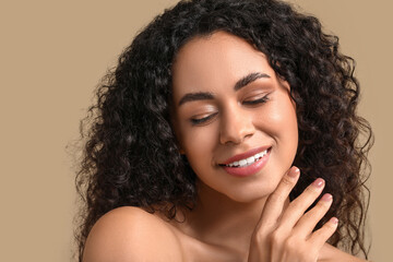 Beautiful young happy African-American woman with healthy skin on beige background