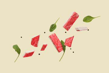 Cut tasty crab sticks with peppercorns and spinach leaves flying on green background © Pixel-Shot