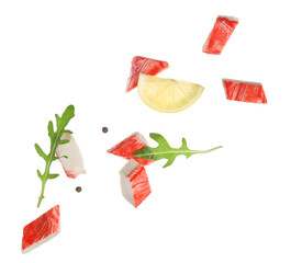 Cut tasty crab stick with arugula leaves, peppercorns and slice of lemon flying on white background © Pixel-Shot