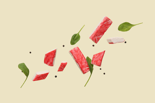 Cut tasty crab sticks with peppercorns and spinach leaves flying on green background