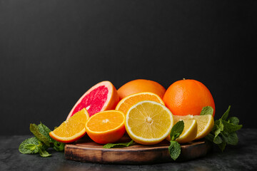 Wooden board with different citrus fruits and mint on black background