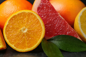 Different citrus fruits with leaves on black background, closeup