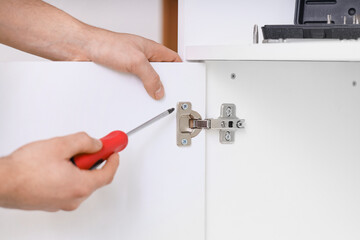 Male carpenter tightening screw in cupboard hinge with screwdriver, closeup
