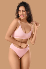 Fototapeta premium Beautiful young happy African-American woman in elegant pink underwear on beige background