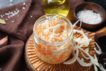 Glass jar with homemade sauerkraut on napkin on black background. Closeup