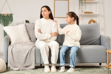 Fototapeta premium Cute girl apologizing to her mother on sofa at home