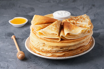 Stack of traditional russian pancakes blini with honey and sour creamon gray background