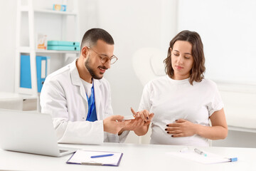 Fototapeta premium Young pregnant woman with doctor using glucometer in clinic. Gestational diabetes concept