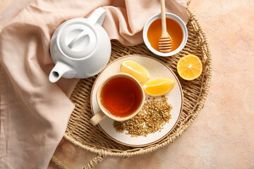 Cup and teapot of hot buckwheat tea with lemon and bowl of honey on beige background