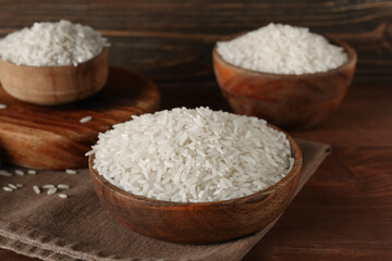 Bowls with raw rice on wooden background