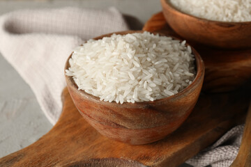 Wooden bowl with raw rice on grey table