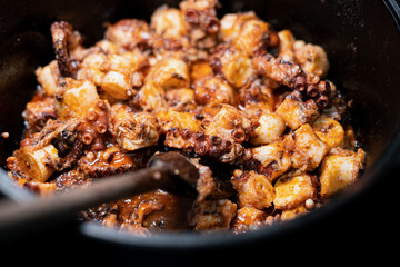 Octopus being cooked with spicys on black iron pan.