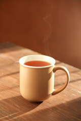 Beige mug of hot tea on wooden table against brown background