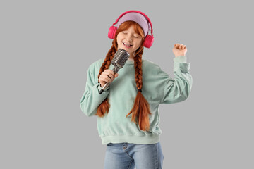 Teenage redhead girl in headphones with microphone singing on light background