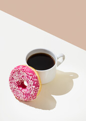 Coffee cup with black coffee and pink frosted donut with sprinkles on a beige and white minimalist background.